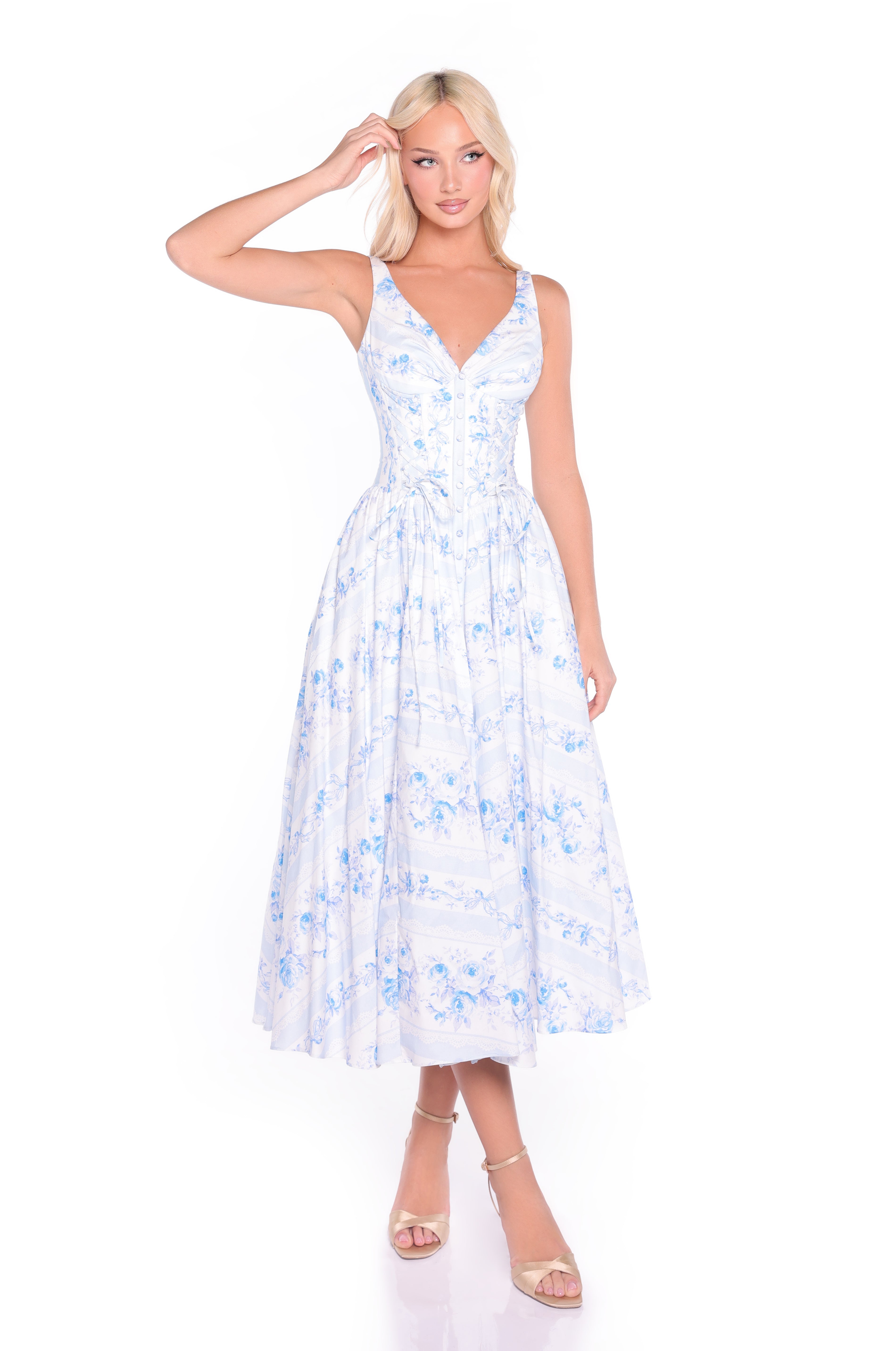 A woman stands against a white background wearing the Ivory & Blue Print Summer Midi Casual Dress: Alina, featuring a sleeveless design, fitted bodice, and flared skirt, paired with strappy heels.